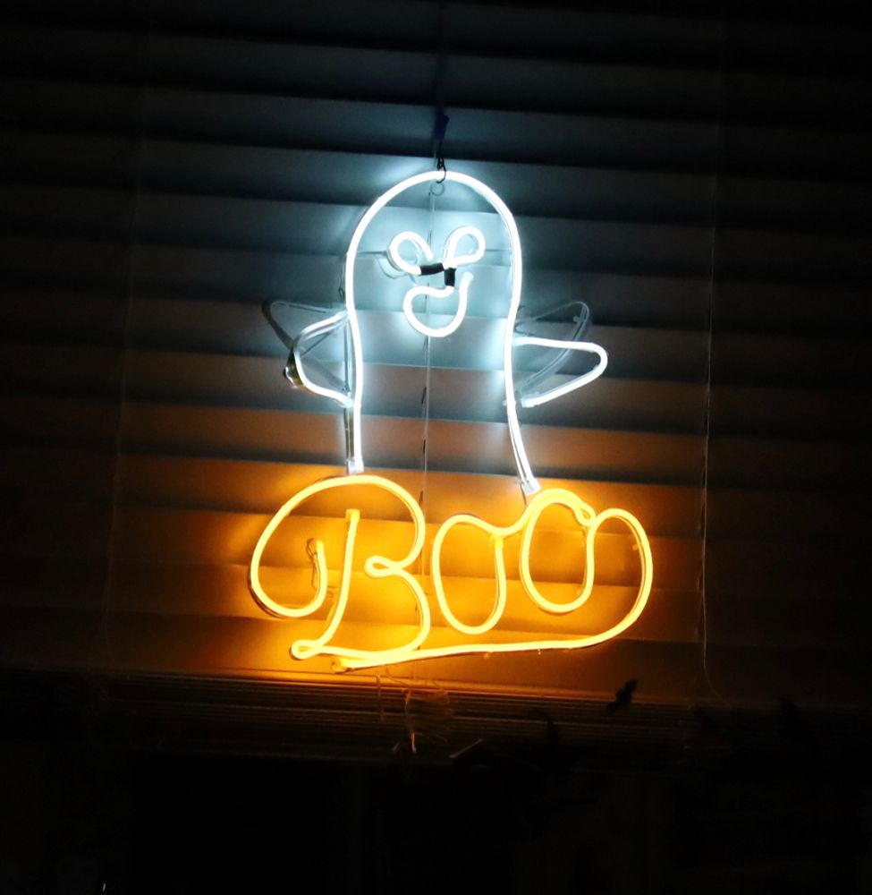 A neon sign of a little ghost with the word Boo underneath hangs in a window. 