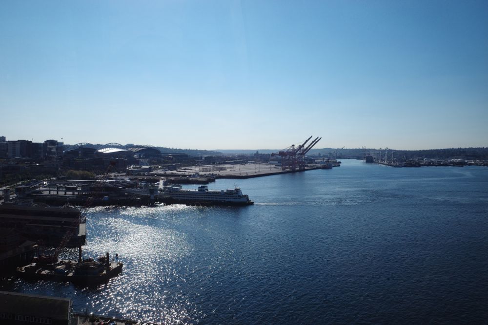 Eastward facing shot of the Seattle waterfront from a high vantage point. Clear blue sky, sparkly water, ferry boat featured