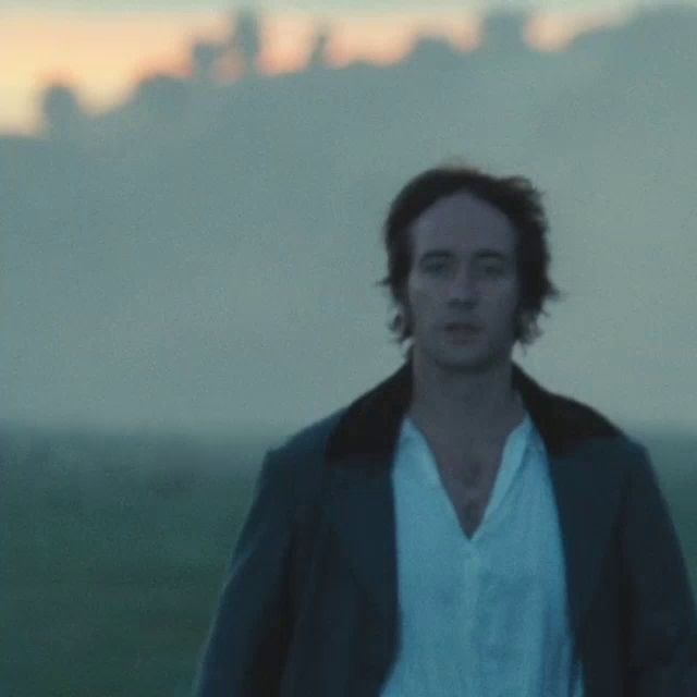a man in a white shirt and a black jacket is standing in a field