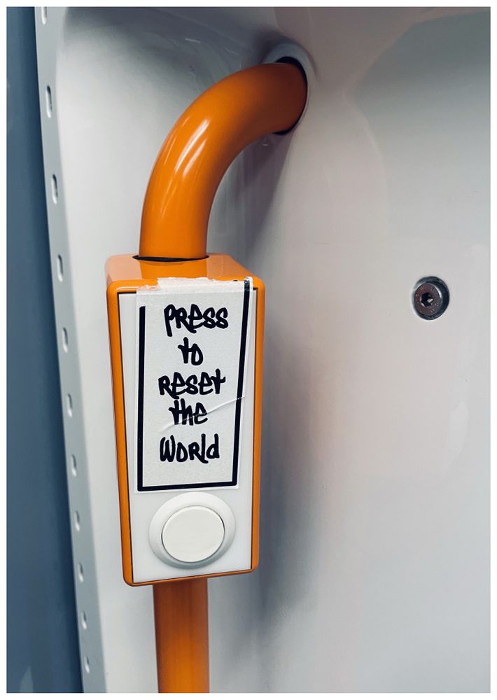 Orangefarbener Tür Öffner in der U-Bahn mit einem Aufkleber mit der Aufschrift: „Press to reset the World“