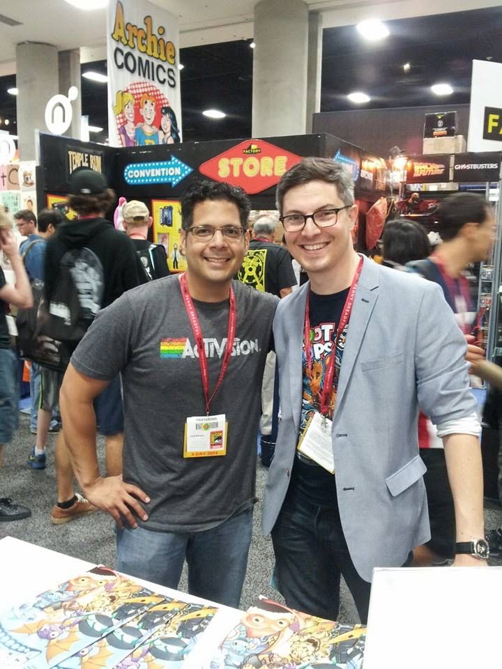 I stand with JP Karliak, voice actor and awesome dude, at the SDCC, IDW booth for the release of the first Skylanders Comic. We are smiling with visible teeth. 