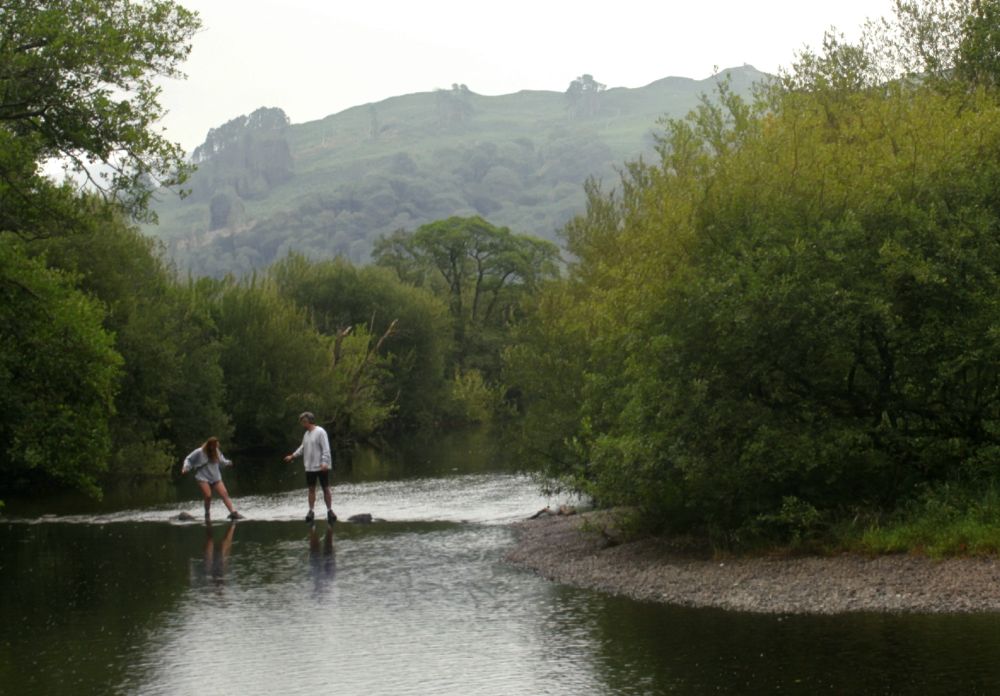 A couple of hikers cross the Rothay River near Rydal in the Lake District.