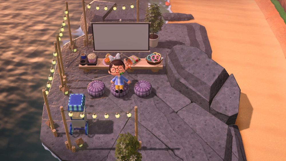 screenshot of animal crossing new horizons showing a small movie set up on an ocean side rock