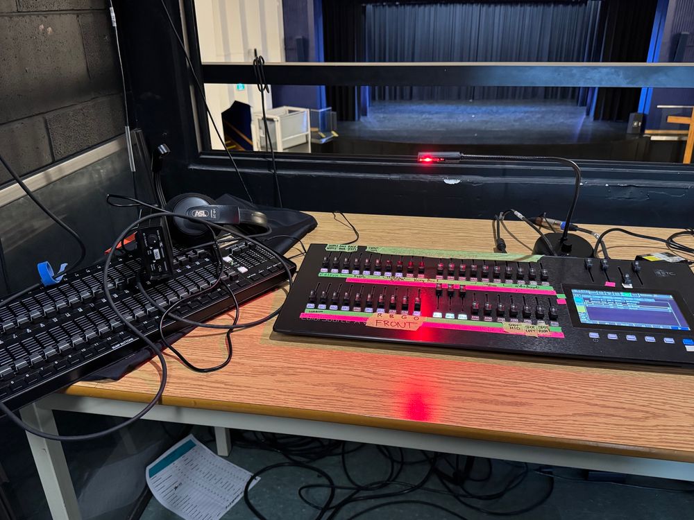 Two lighting consoles. In the background, a stage. 