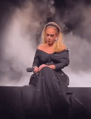 a woman in a black dress is sitting on a stage holding a microphone and crying .