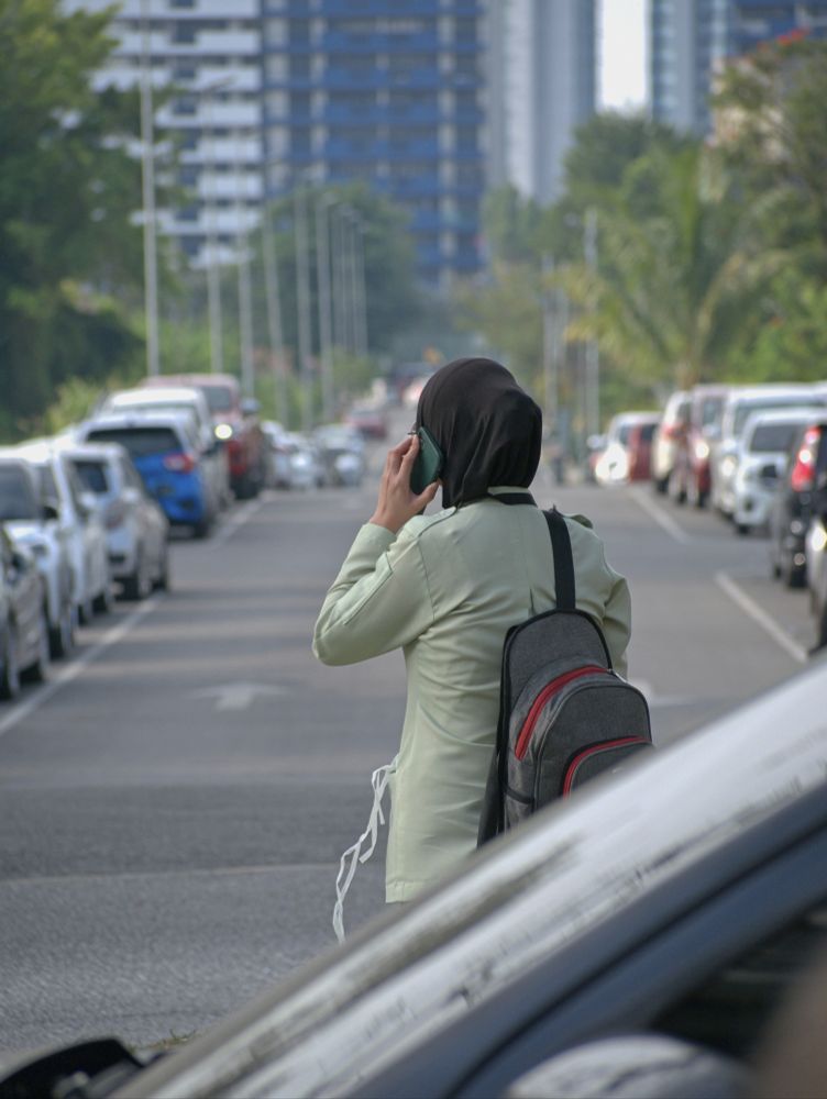 A lady's back, in green, while holding a phone