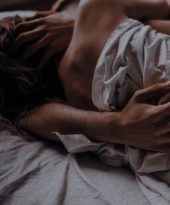 Image of a couple in bed. They are embracing each other under the crinkle of sheets, one hand around her body while the other cradles her face
