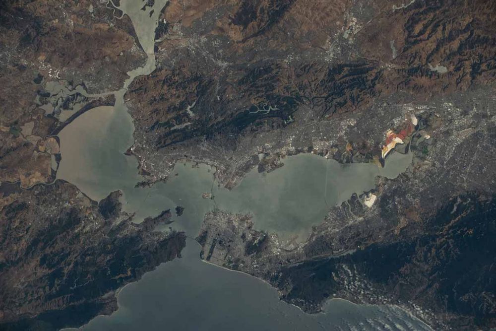 Vue aérienne de la baie de San Francisco, montrant des étendues d'eau, des terres urbaines et des zones montagneuses environnantes.