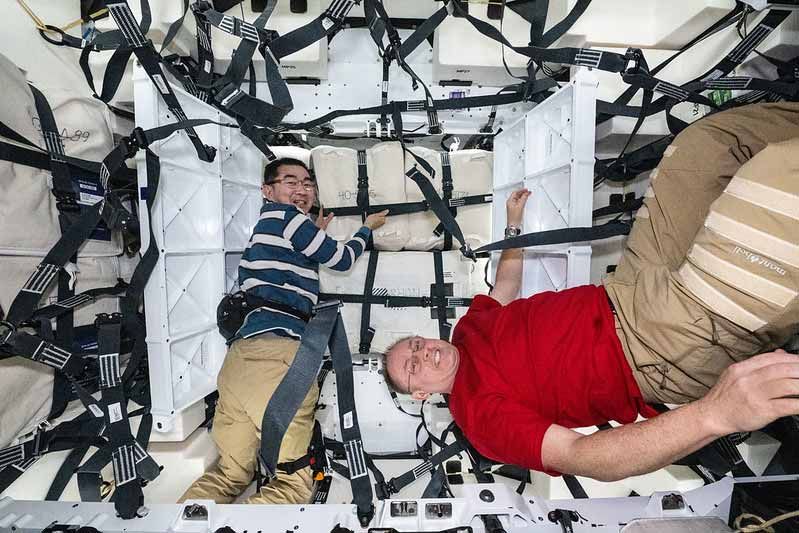 Deux astronautes flottent en apesanteur à l'intérieur d'un vaisseau spatial, entourés de sangles et équipements.
