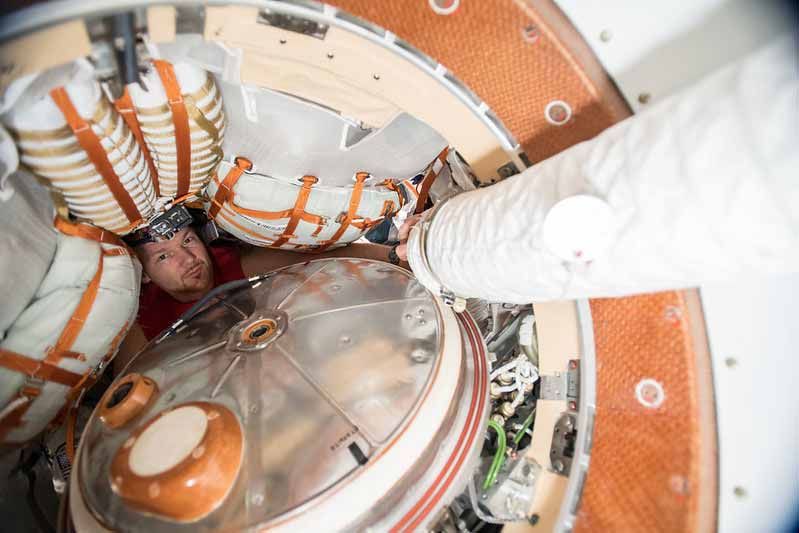 Un astronaute travaille à l'intérieur d'un module spatial, entouré d'équipements et de câbles.