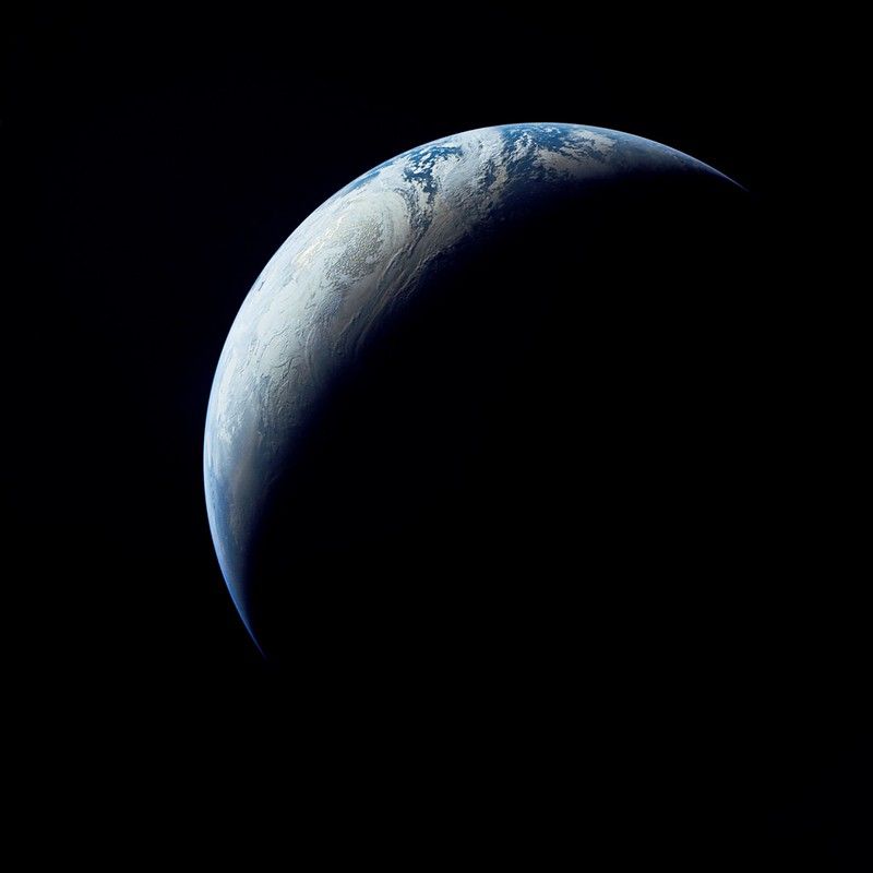 Vue partielle de la Terre depuis l'espace, illuminée à moitié par le soleil, montrant des nuages et des océans sur la surface visible.