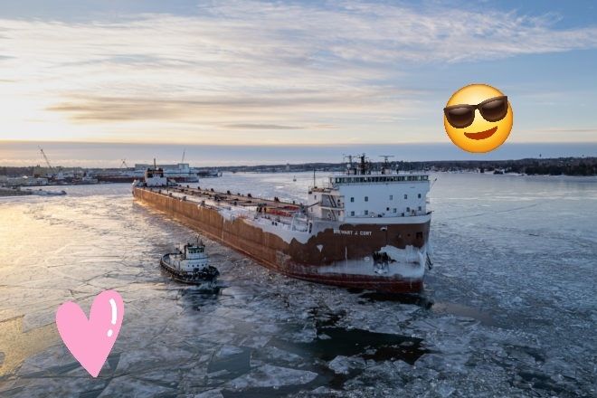 A photo of the lake freighter Stewart J Cort on an icy lake, decorated with a sunglasses emoji and a cartoon heart