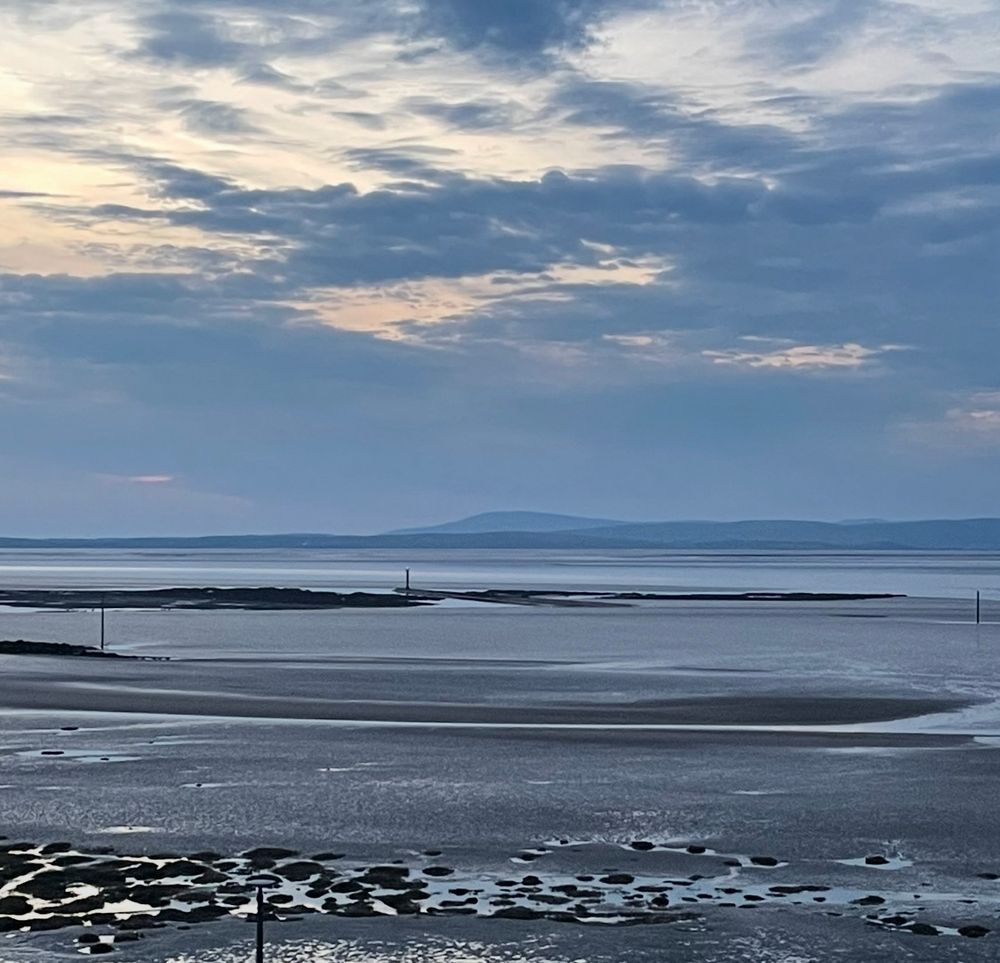 Morecambe Bay wet sand, rocks and poles in the foreground. The summit of Black Combe rises behind the Furness Peninsula in the centre of the photograph. 