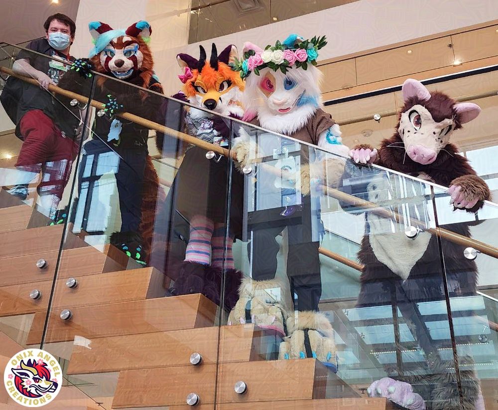 Image of 4 fursuiters on brown stairs, looking down at the viewer