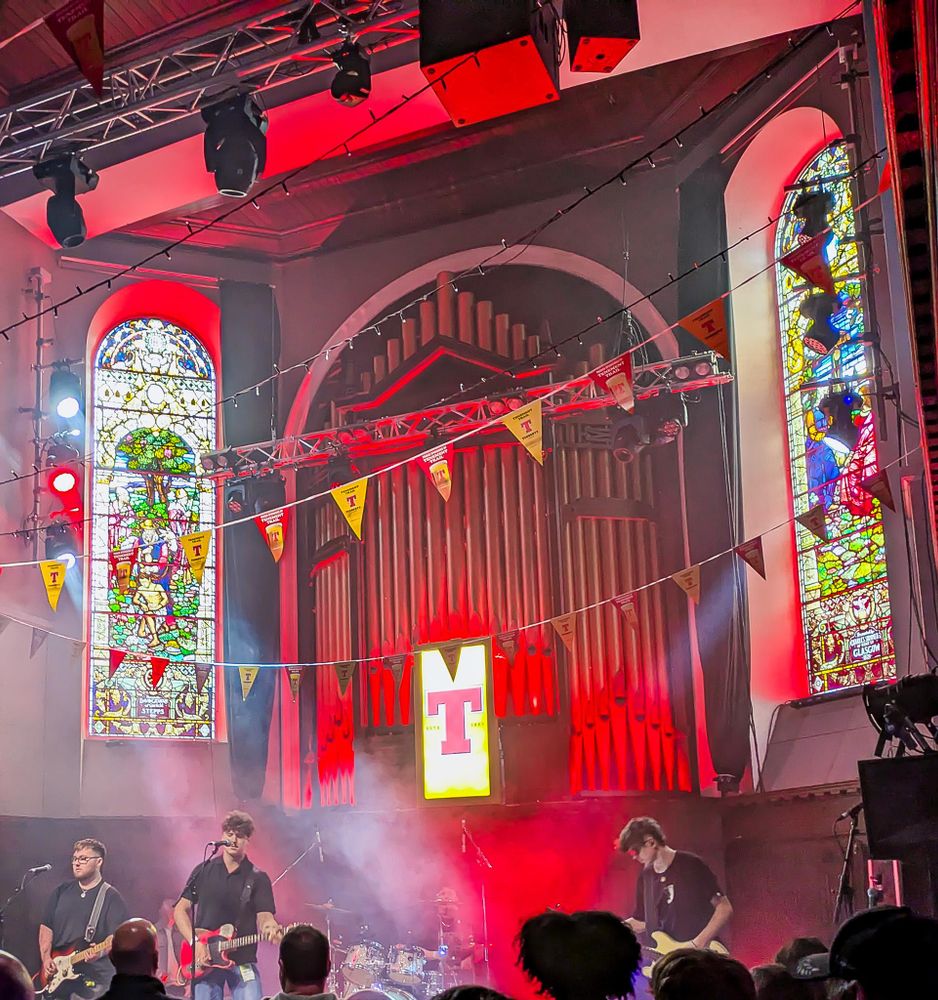 A band on stage in a converted church with stained glass windows.