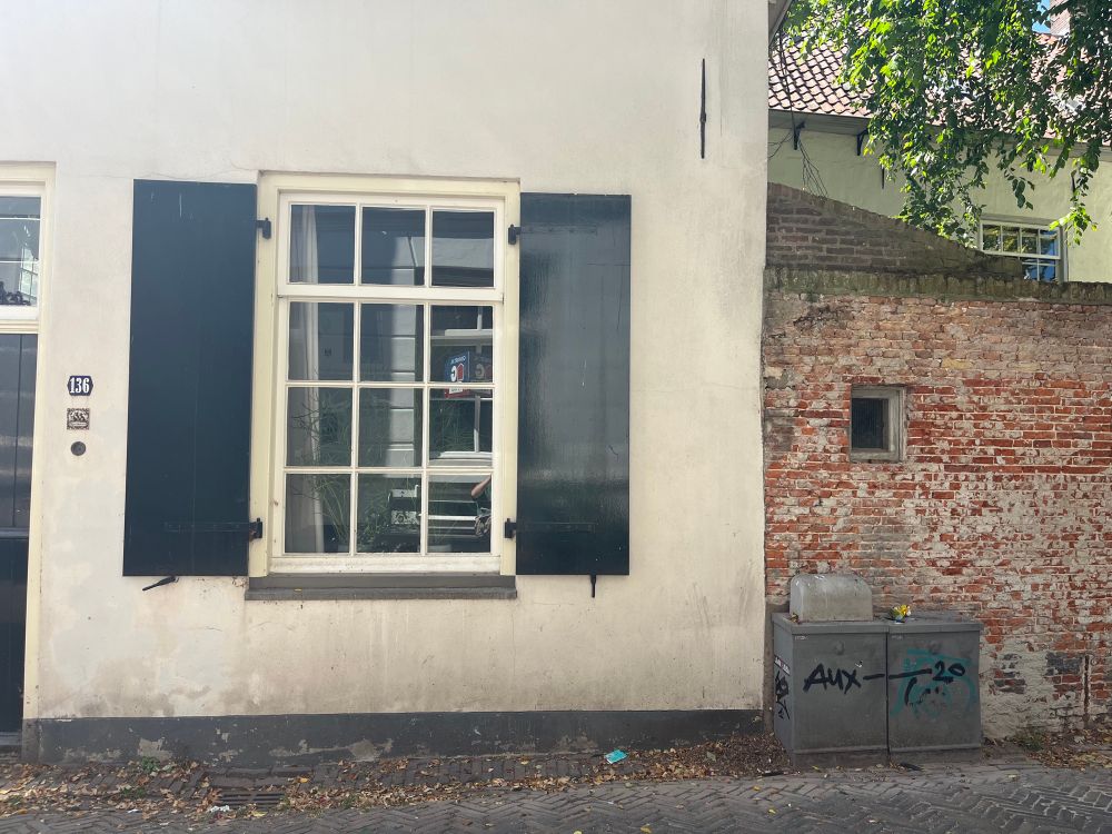 Photo of sketched scene, on the left a window in a white plastered wall, to the right a high old red brick wall that surrounds a garden. 