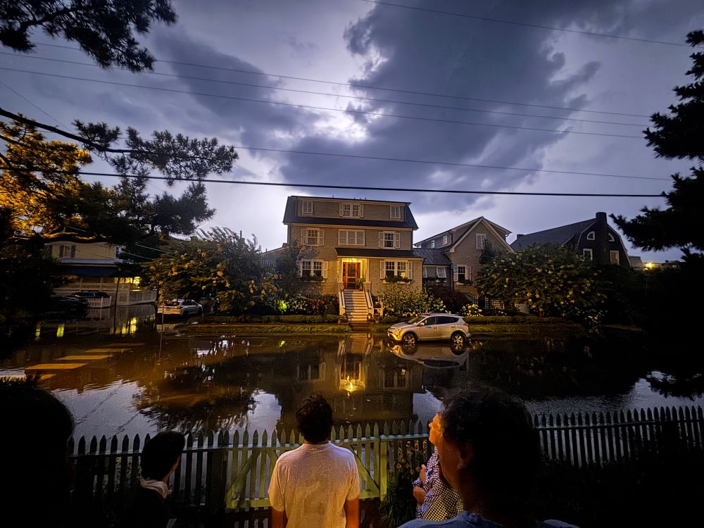 Lightning-illuminated night sky over flooded street as people look on