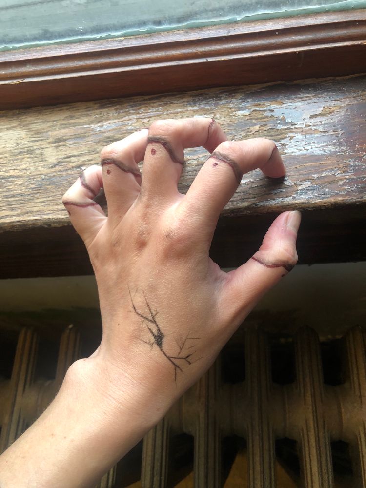My hand clawing at a window cell. The fingers are painted to appear as though they have doll joints, and the back is painted to look like chipped porcelain.