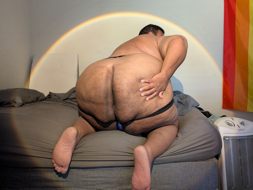 Superchub wearing a jockstrap bent over on all fours on his bed showing off by reaching back with one hand spreading his massive butt cheeks