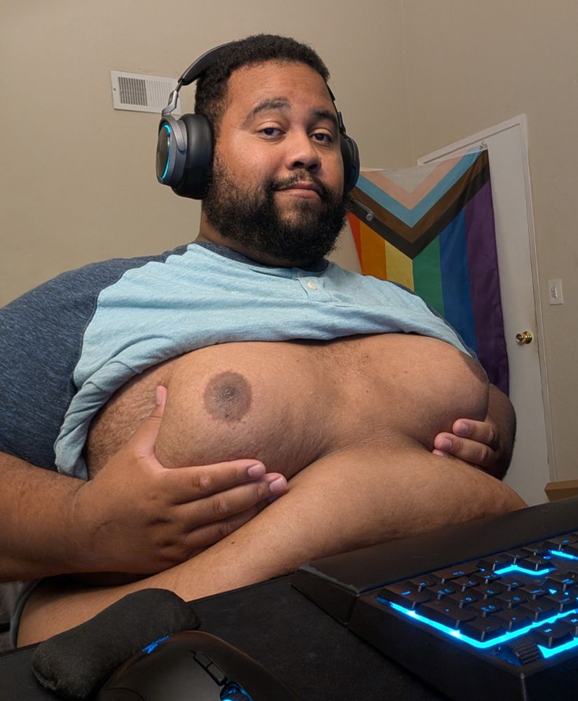 Superchub sitting with his shirt rolled up cupping his fat moobs and pushing them together 