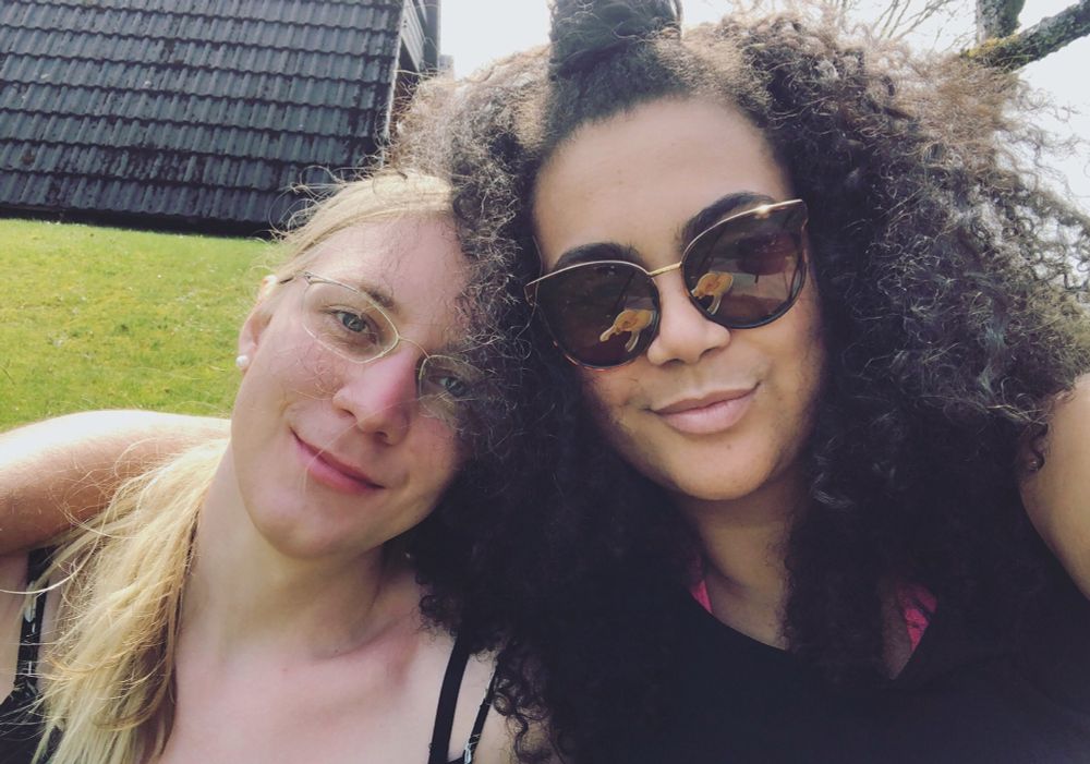 
Charlotte and Joy sitting outside on the lawn. Joy has their arm around Charlotte’s shoulders. Both are smiling.