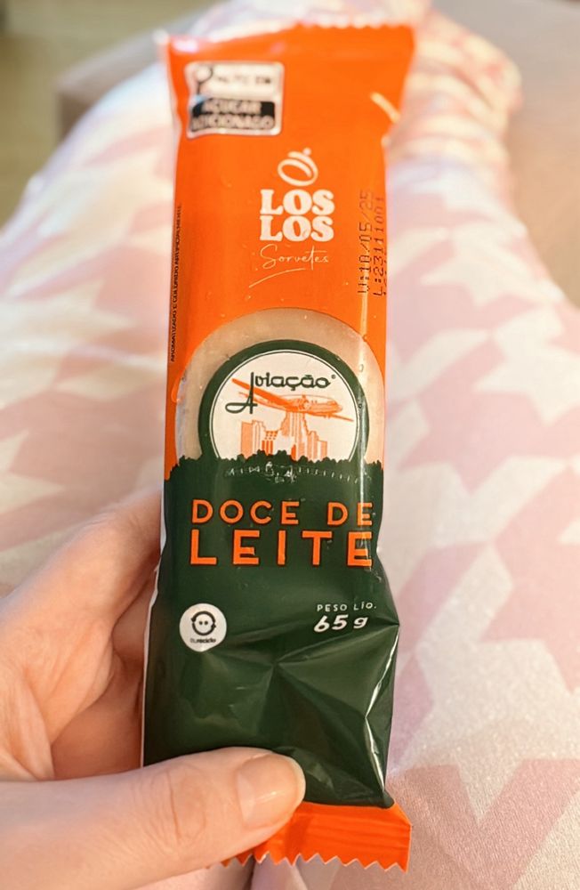 Minha mão segurando um picolé de doce de leite da marca Aviação.