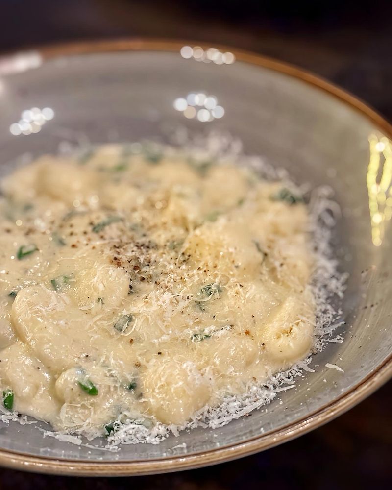 Um prato de nhoque com molho branco com três queijos e cebolinhas verdes. Salpicado com parmesão ralado fino.