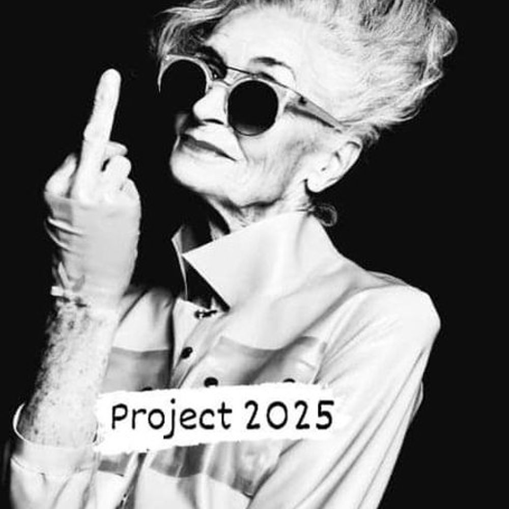 Black and white photo of a very hip elder woman wearing a light colored shirt with snaps and a popped collar, in John Lennon sunglasses , giving the finger. Caption overlaid reads Project 2025. 