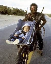 Tex Cobb as the Lone Biker of the Apocalypse, Leonard Smalls in the film Raising Arizona; pictured here with a baby in a car seat strapped to the front of his motorcycle 
