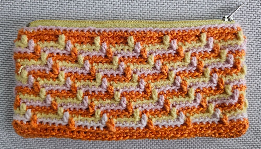 Crocheted purse with zipper. The pattern shows stripes in orange, yellow and pale pink. 