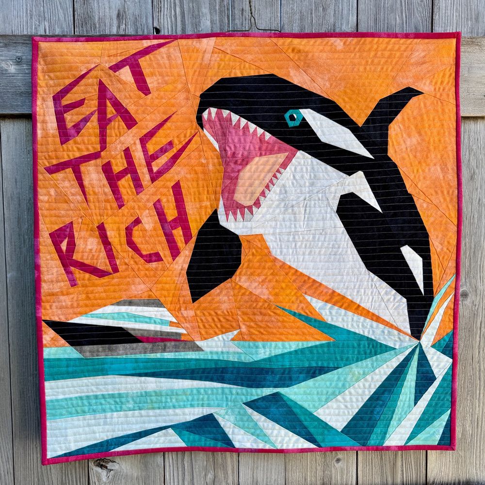 My Eat The Rich quilt, depicting an orca jumping out of the water to chomp on a yacht. 