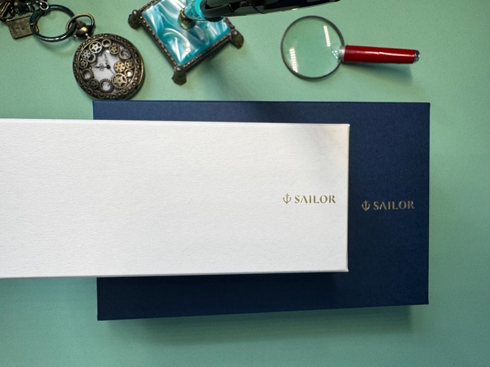 Two Sailor fountain pen boxes and some desk ephemera: pocket watch, magnifying glass, and a pen holder.