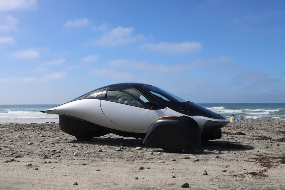 A side-profile view of the Aptera on a beach on a sunny day.
