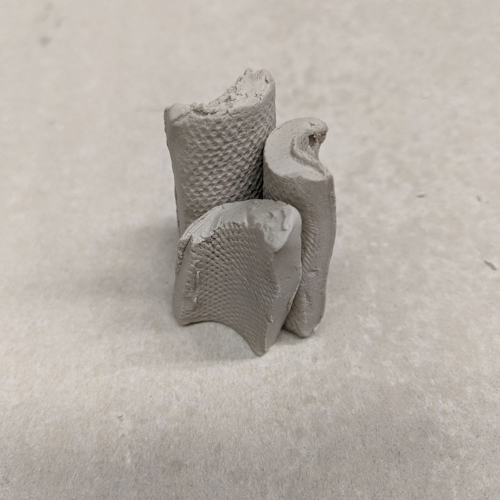 A photograph of a clay sculpture composed of three elongated half circles of differing height arranged back to back