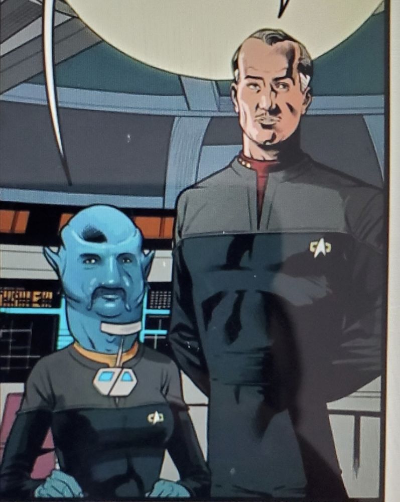 A picture from a Star Trek comic. A Caucasian middle aged male captain with a receding hairline stands next to a female Benzite operations officer,who is seated at a console. The comic book artist has drawn the Benzite with a disproportionately large head for the body, with a neck that bulges out of her uniform's collar. 