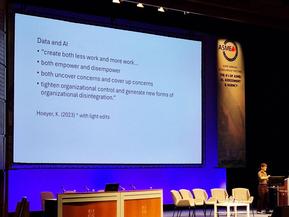 Margaret standing at podium with a slide protected behind her. Text on slide-

Data and Al
• "create both less work and more work..
• both empower and disempower
• both uncover concerns and cover up concerns
• tighten organizational control and generate new forms of organizational disintegration."

Hoeyer, K. (2023) * with light edits


