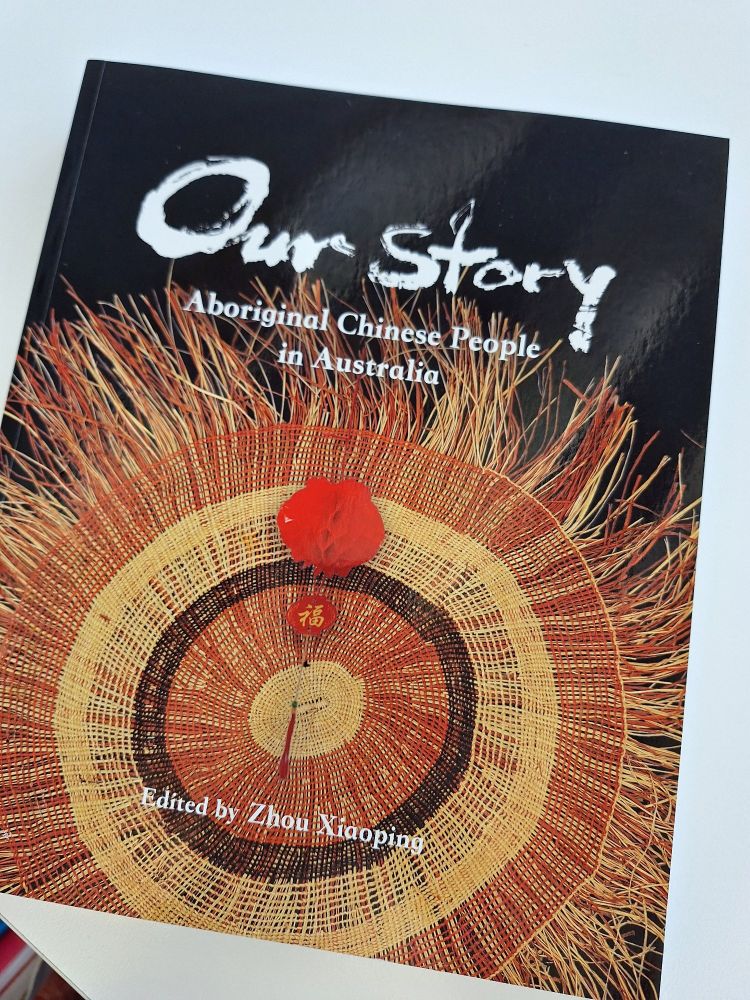 The cover of the book, featuring an Aboriginal red, black and yellow twined mat, decorated with a Chinese hanging charm typically used at Chinese New Year with the character for 'fortune'.
