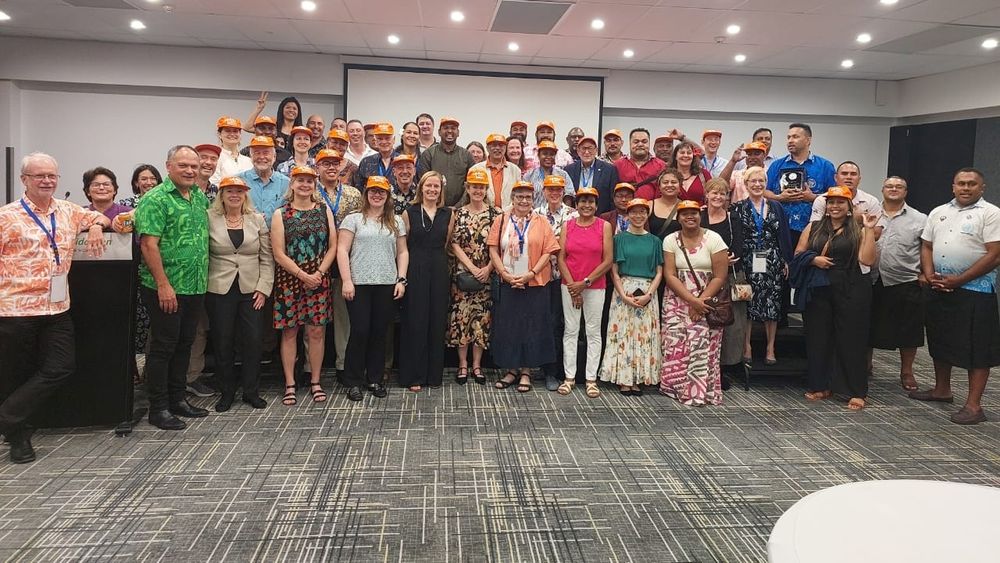 A picture of perhaps 50 people in colourful outfits posed for a group photo in a meeting room, many wearing orange G4 caps and/or traditional dress.