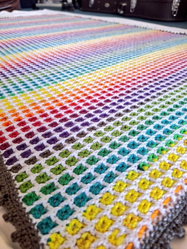 A crochet blanket in super-bright rainbow shades, pinned out on a sheet to dry into shape.