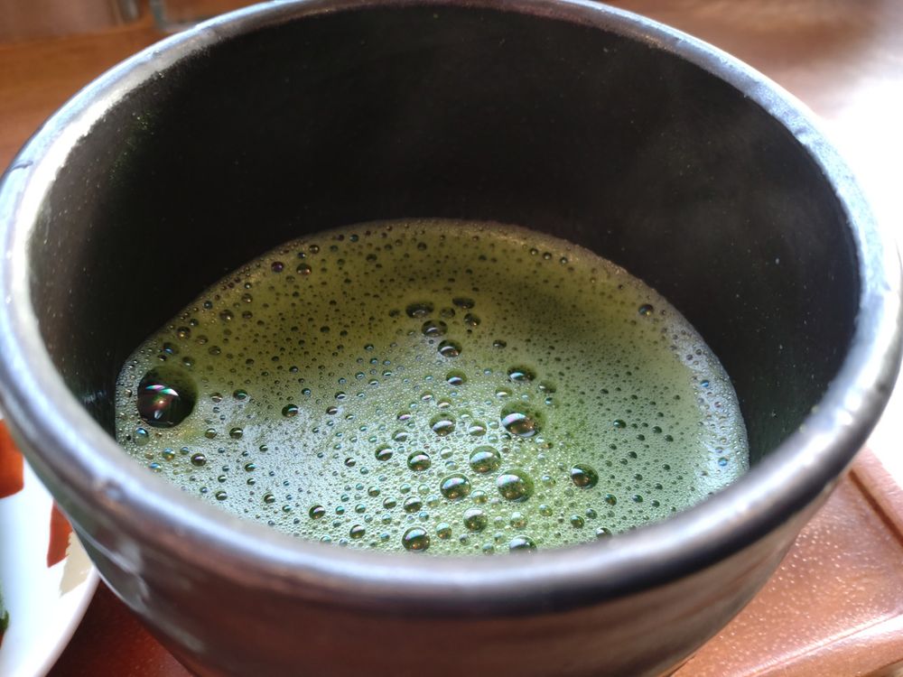 大きな茶道などで使う器に入った温かいお抹茶。泡立つ緑の水面から、わかりにくいが薄く湯気が立っている。