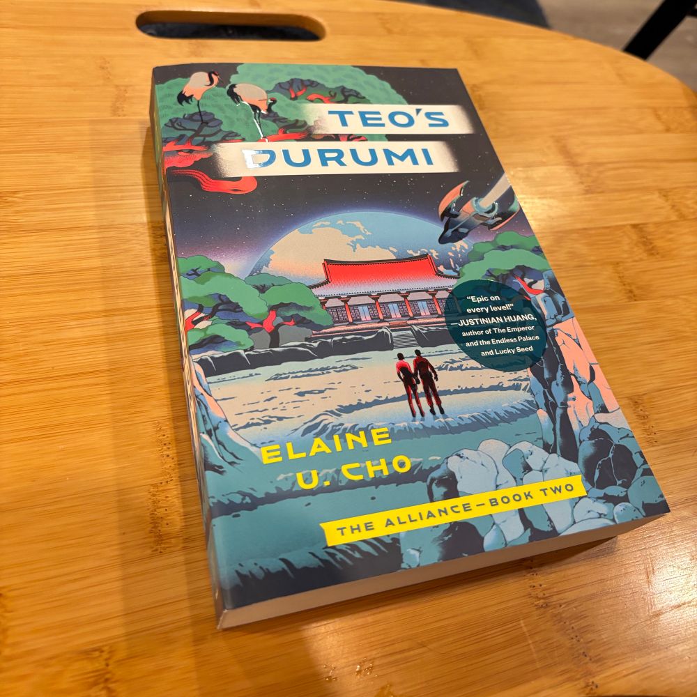 A copy of Teo’s Durumi by Elaine U. Cho. The cover shows two figures standing on the lunar surface in front of a house and garden, with the earth rising in the background.