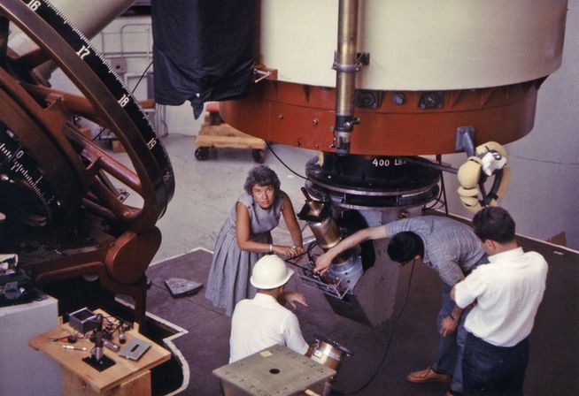 Vera Rubin working at Lowell Observatory in Flagstaff, Arizona, in 1965. This photograph was taken the same year Rubin joined Carnegie Science as a Staff Scientist, a position that freed her from teaching obligations and allowed her to focus entirely on research and observation. Rubin’s longtime research partner Kent Ford appears with his back to the camera in a white hard hat. This was one of their first observing runs together. Credit: Carnegie Science