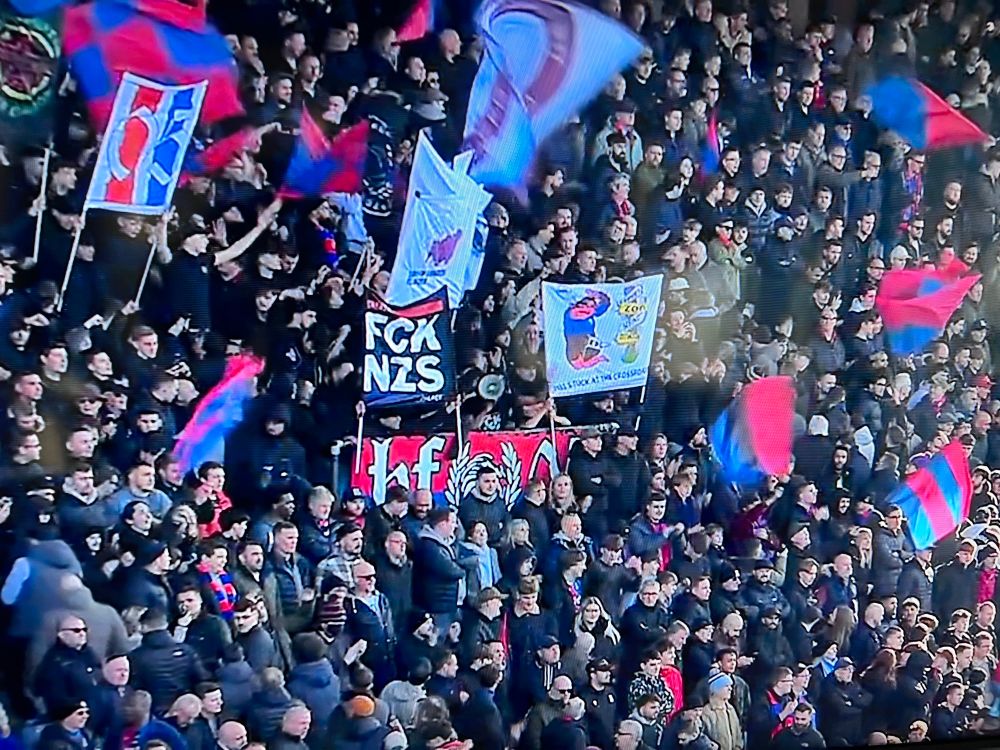 The Holmesdale Fanatics waving flags and holding two-poles, one of which reads “FCK NZS”