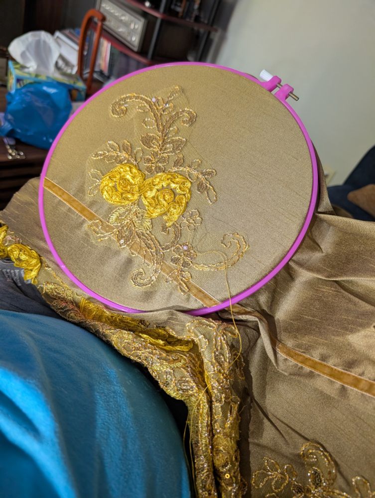 Gold fabric in an embroidery hoop with a yellow lace flower centered in the hoop