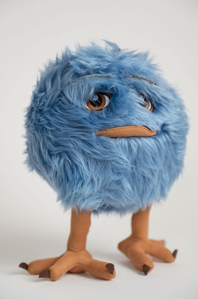 A stuffed Blue Meep toy. a round fuzzball with eyes, lips, and two birdlike legs.