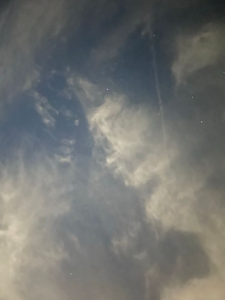 A few stars peek through whispy clouds at night.