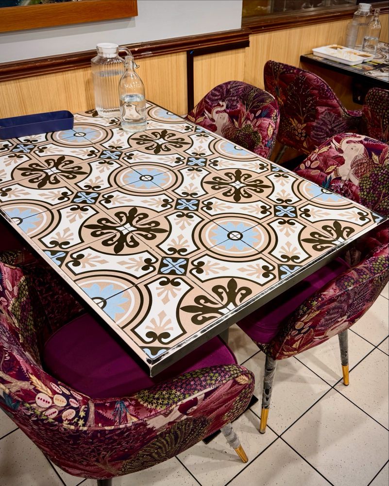 a table with a highly decorated top that looks like patterned tiles with seats upholstered in a highly patterned red fabric