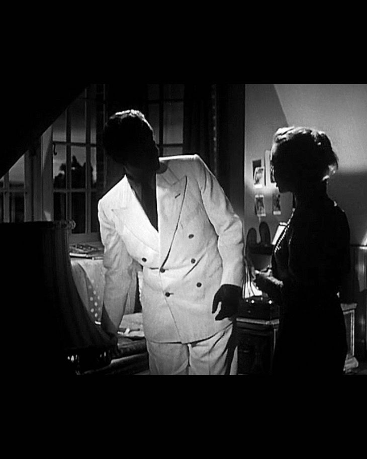 black and white still from a film showing a man wearing a suit in a darkened room, the white fabric glowing