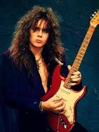 Yngwie Malmsteen holding a red Fender Stratocaster with a maple fretboard and cream pickguard.