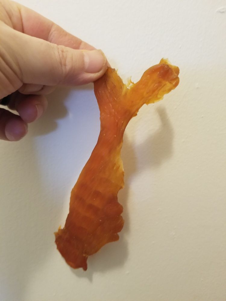 Hand holding vaguely fish shaped piece of chicken jerky.